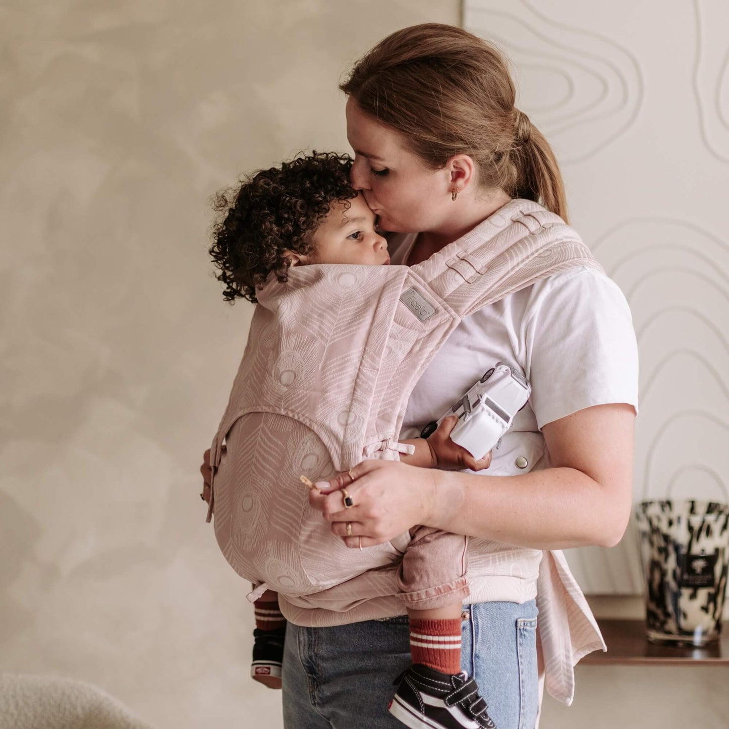A toddler is carried in Fly Tai Mei Tai Sling baby carrier Design Feather rose
