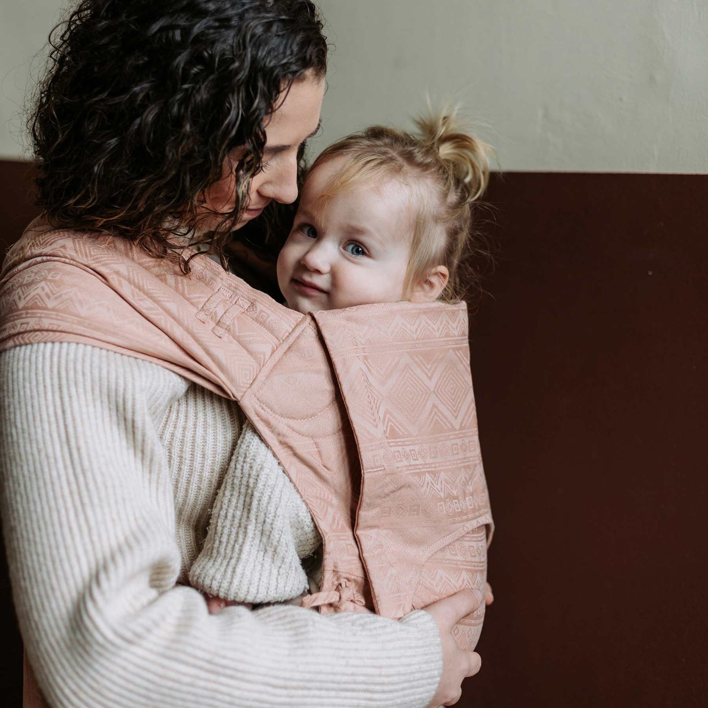 A baby is carried in Fly Tai Mei Tai Sling baby carrier Design Cubic Lines tuscany