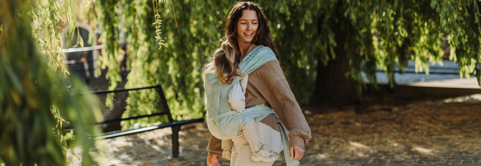 A mother is carrying her toddler in a FlyTai Blue Feather baby carrier in a park
