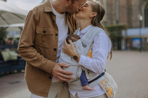 Two parents are kissing each other. The mother is carrying her baby in a FlyClick cubic lines pale grey.